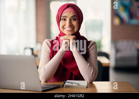 Attractive young woman in headscarf student using laptop at cafe Stock Photo