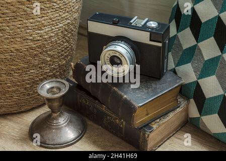 Old photo camera placed on top of the old books surrounded by silver candlestick and blue aqua cusson. France Stock Photo
