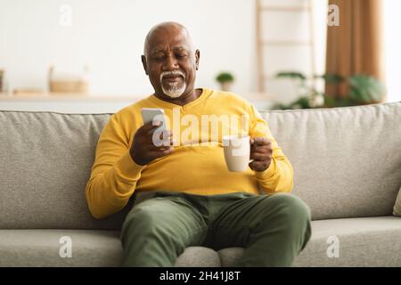Mature African American Male Using Cellphone Texting Sitting At Home Stock Photo