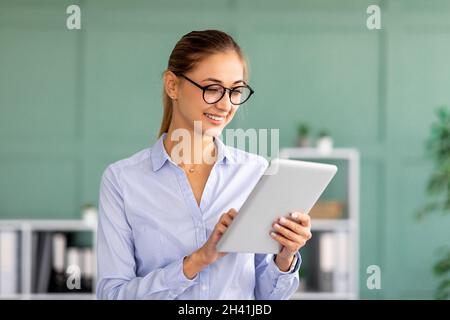 Happy business lady using digital tablet at her workplace in office interior, reading documents online, checking email Stock Photo
