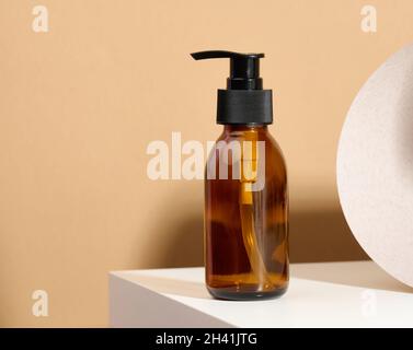 Brown glass bottle with black pump of cosmetic products on white table. Natural organic spa cosmetic, beauty concept. Mockup Stock Photo