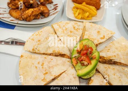 Mexican quesadillas stuffed with chicken tinga stew with ripe avocado, a tablespoon of pico de gallo and other dishes in the background Stock Photo