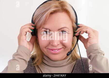 Close-up portrait of smiling middle-aged caucasian woman adjusting a headset on her head. Stock Photo