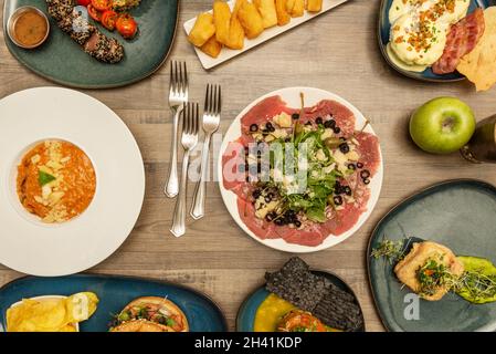 set of international dishes with beef carpaccio, eggs benedict, fried yucca, risotto with parmesan, salmon tartare, green apple and forks Stock Photo