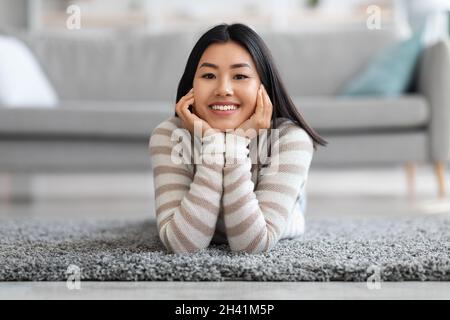 Portrait Of Beautiful Young Asian Female Relaxing On Floor In Living Room Stock Photo