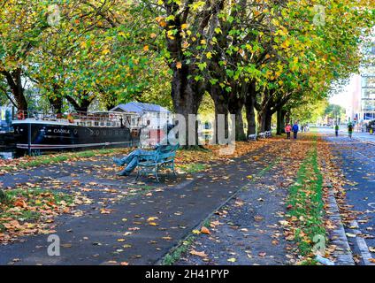 Autumn at Grand Canal, Dublin, Ireland with colorful leaves on trees and bank. Bench sculpture of poet 'Patrick Kavanagh'. People walking and cycling Stock Photo