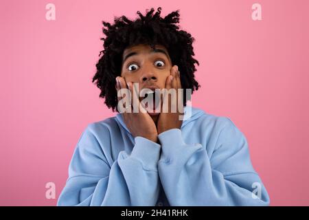 Cool black teen guy touching his face, screaming in terror on pink studio background Stock Photo