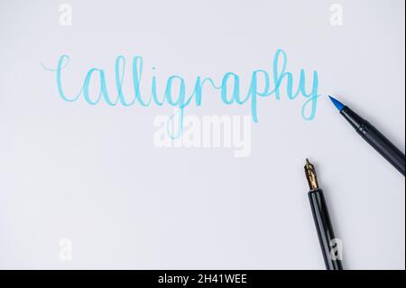 brush pen lying on a white paper, where is written the word calligraphy Stock Photo