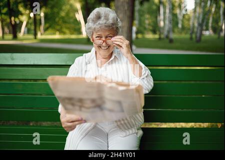 An elderly woman in glasses reading newspaper Stock Photo
