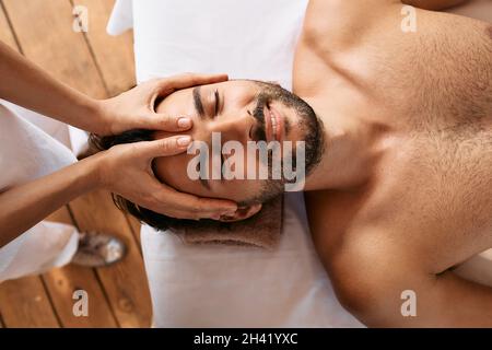 Relaxing anti-stress head massage. Handsome man relaxes in a massage parlor during head massage, top view Stock Photo