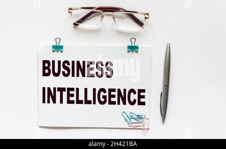 Business analytics, the text is written on a notebook. Nearby lie a pen, glasses and paper clips on a white background. Stock Photo