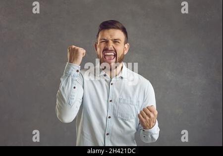 Portrait of an emotional young man laughing and shouting with clenched fists celebrating victory. Stock Photo