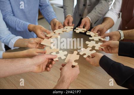 Team of business people standing around office table putting together pieces of jigsaw puzzle Stock Photo