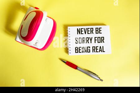 Never be sorry for being real. Inspirational phrases on a notepad, next to a stapler and a pen on a yellow background. Personal development concept Stock Photo