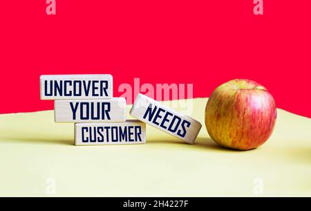 reveal the needs of your customers. Text on wooden blocks and red and yellow background with apple Stock Photo