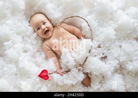 Cute smiling caucasian baby cupid on white clouds background with bow and heart arrow. Happy Valentines day concept. Stock Photo