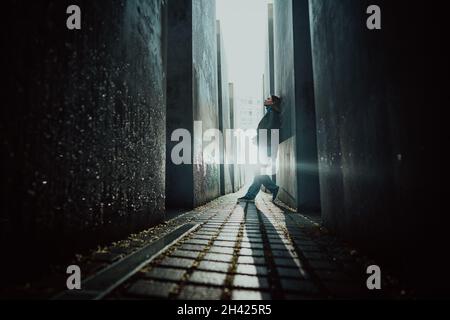 October 2021 - Berlin, Germany. Woman stands in dark maze between tall blocks in Holocaust Jewish Memorial of Murdered Jews. Light at the end of Stock Photo