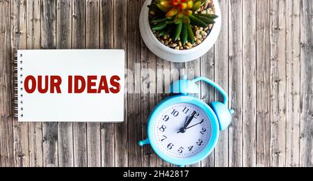 Place of work. Alarm clock, cactus and paper with the text OUR IDEAS on a wooden table. Stock Photo