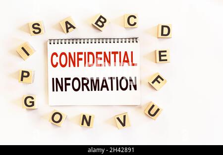 CONFIDENTIAL INFORMATION is written on a notebook next to wooden cubes with letters. Business concept Stock Photo