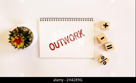 OUTWORK , the text is written on a notebook and a white background. On the table are wooden cubes with signs and there is a cactus flower Stock Photo