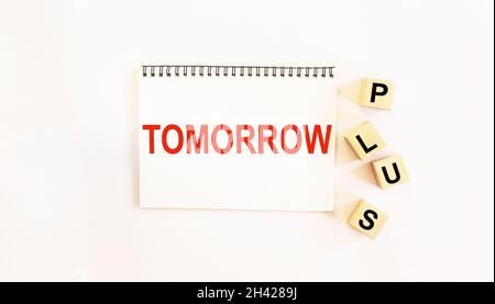 Notepad on a white background with the writing of the text TOMORROW, wooden cubes with the word PLUS lie next to Stock Photo