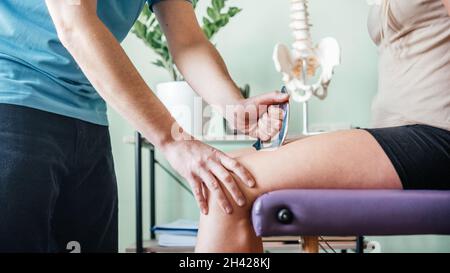 Therapist using IASTM instrument treatment, girl receiving soft tissue treatment on her leg with guasha stainless steel tool Stock Photo