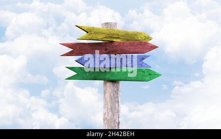 Four colored wooden arrows pointers yellow, red, blue and green. Blue sky background with clouds. Stock Photo