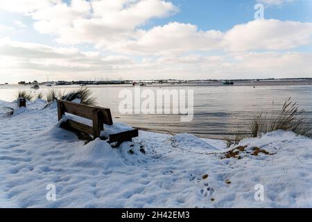 A snow covered bench with a view to the beach and River Deben at the popular visitor Bawdsey Quay on the Suffolk coast Stock Photo