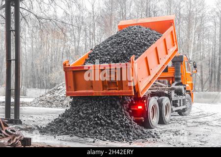 Dump truck in the industrial zone unloads coking coal from the body. Stock Photo