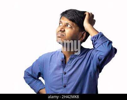 A young Indian male in blue dress scratching head and thinking on white background Stock Photo