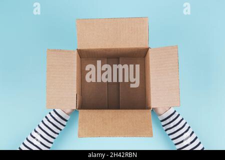 Top view to woman hands holding open empty brown cardboard box on light blue background Stock Photo