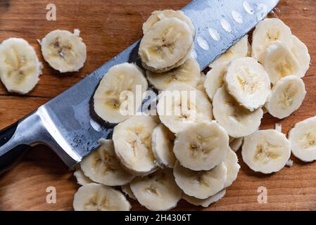 Sliced banana lying on a cutting board next to a knife. Stock Photo