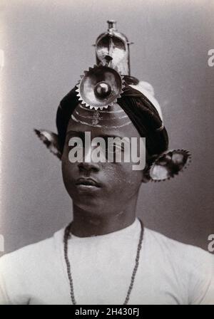 A young Indian man, wearing an elaborate headress and makeup, in a studio setting. Photograph, ca.1900. Stock Photo