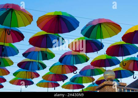 Many colorful umbrellas hang in the sky above the cafe. Decorating the street with umbrellas. Stock Photo