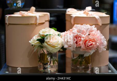 Two bouquets in a vases. beautiful flowers in pots. Transparent glass vases and artificial fake roses flowers on a pink gift boxes background. Valentin Stock Photo