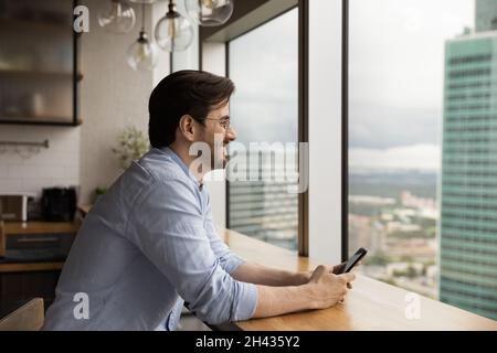 Dreamy happy young caucasian man holding cellphone in hands. Stock Photo