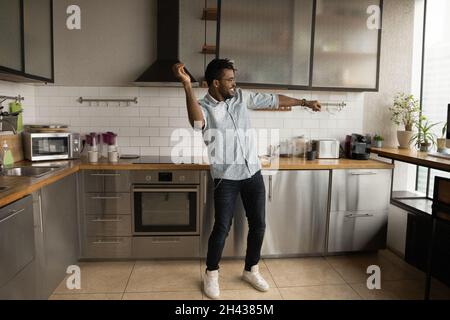 Happy handsome young african american man dancing in kitchen. Stock Photo