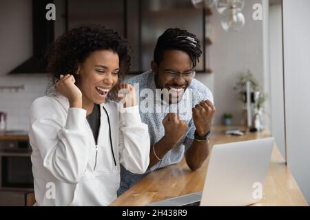 Overjoyed laughing young african couple celebrating internet success. Stock Photo