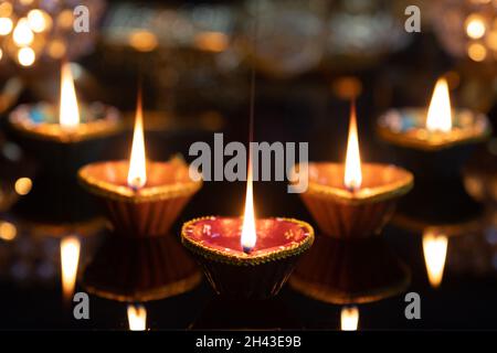 Happy Diwali Clay Diya Deep Dia Glowing lamps arranged on a reflective base Laxmi pooja Deepawali, with glittering background bokeh Stock Photo
