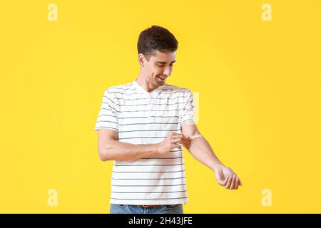 Young man applying plaster onto his arm on yellow background Stock Photo