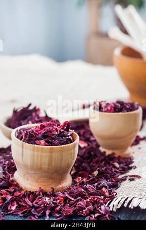 Dry hibiscus tea in wooden spoon and small cups on a table with straw mat Stock Photo