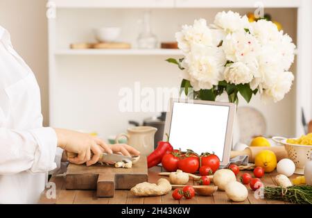 Woman cutting mushrooms and recipe book on table in kitchen Stock Photo