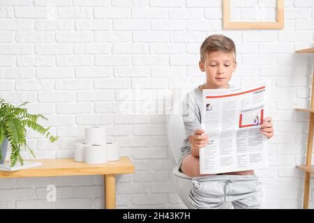 Little boy reading newspaper while sitting on toilet bowl in bathroom Stock Photo