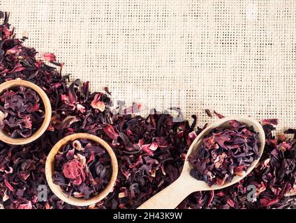 Straw mat background with hibiscus tea. Wooden spoon and small cups with dry  hibiscus petals. Flat lay, top view, copy space Stock Photo