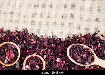 Straw mat background with hibiscus tea. Wooden spoon and small cups with dry  hibiscus petals. Flat lay, top view, copy space Stock Photo