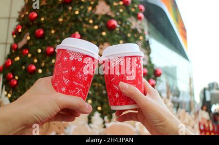 Holiday Theme Takeaway Coffee Cup in Couple's Hands against Blurry Christmas Tree Stock Photo