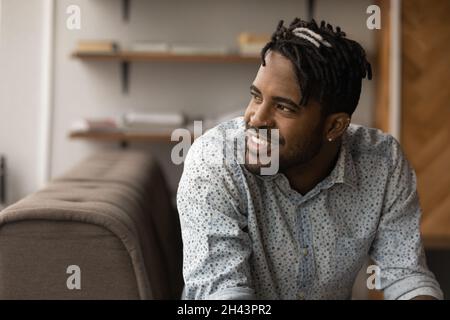 Happy young african ethnicity man dreaming resting on sofa. Stock Photo