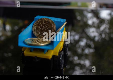 A yellow turquoise colored toy truck carrying and dropping off some bitcoins.  Stock Photo