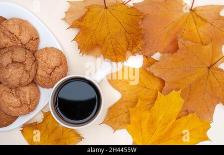 flat lay of autumn yellow maple leafs, cup with hot tea, white plate with cookies on ivory background Stock Photo