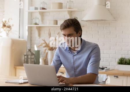 Handsome thoughtful man sit at table working on laptop Stock Photo